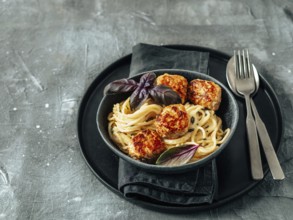 Zucchini Parmesan Meatballs with Pasta Carbonara in black craft plate over gray background. Close