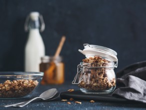 Homemade granola in glass jar on dark table. Ingredients for healthy breakfast - granola, milk and