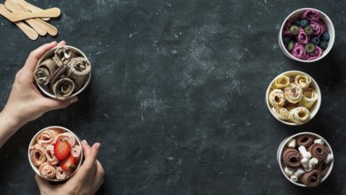 Hands with rolled ice cream in cone cups on dark background. Different iced rolls top view or flat