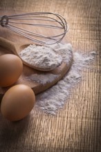 Flour in spoon eggs and corolla on vintage wooden board food and drink concept