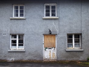 An old abandoned grey derelict house on a residential street with dirty broken windows and a