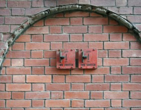 Two old red metal fire switches on an exterior brick wall