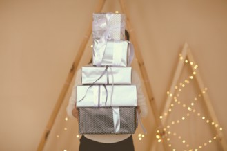 Female holding big stack of presents wrapped in brown paper with white bows on simple background