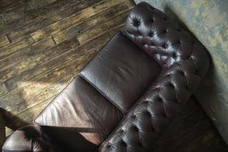 Top view of a vintage tufted leather couch against a wooden floor and textured wall
