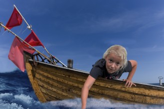 Child in a wooden boat with waves and holding his hand in the water