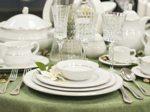 Set of new dishes on table with green tablecloth. Stack of white plates with flowers on restaurant