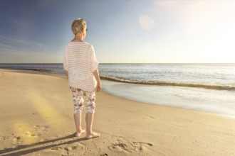 Older woman standing at the beach and looking towards the ocean with scenic lens flare