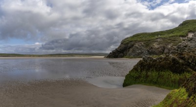 View of the picturesque golden sand Maghera Beach with algae-covered rocks and cliffs in the