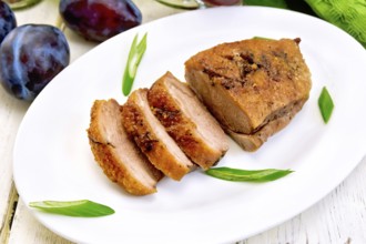 Roasted duck breast with green onions in a white oval plate, towel and plums on a background of