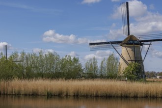 A traditional windmill in a wide landscape with meadow, water and cloudy sky on a summer's day,