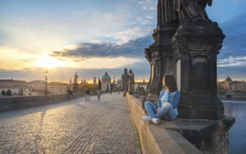 Young brunette woman, sitting relaxed on the Charles Bridge walls, over the Vltava river, admiring