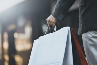 Close up of a young caucasian man holding some different paper shopping bags in the street
