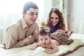 Naked baby with her parents lying on soft blanket in the room