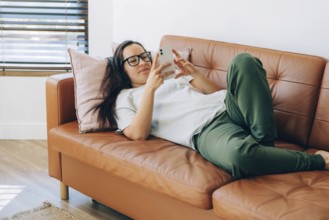 Junge moderne Frau Freiberufler auf dem Sofa liegend tippt Nachrichten auf dem Smartphone
