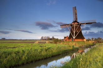 Dutch windmill reflected in river in morning sunrise sunlight, Holland
