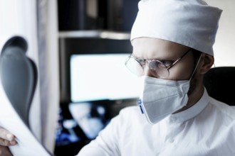 Doctor wearing protective gear, concentrating on a document, displaying analytical focus