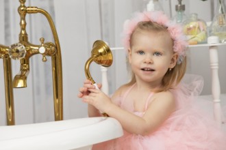 Little funny girl in a smart pink dress in the bathroom