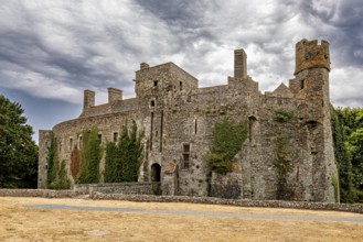 Stone castle with towers and ivy in front of a cloudy sky, Pirou Castle in Normandy, France