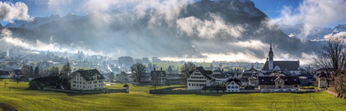 Panorama over the village of Schwyz, Switzerland with wisps of fog and clouds in oblique sunlight,