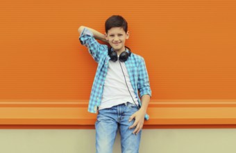 Portrait of happy modern teenage boy listening to music with headphones in the city on orange wall