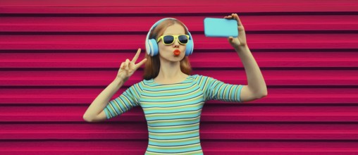 Summer portrait of stylish young woman taking selfie with smartphone listening to music with