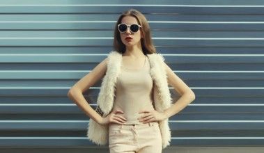 Portrait of modern stylish young woman in white fur vest, glasses, fashionable female model posing