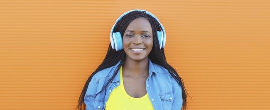 Portrait of happy African young woman listening to music with headphones, cool modern black teenage