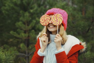 Winter portrait of happy funny smiling young woman having fun with sweet lollipop wearing hat