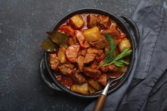 Beef meat stew with potatoes, carrot and delicious gravy in black casserole pot with bay leaves and
