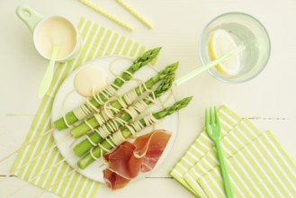 Steamed green asparagus on wooden skewers with spaghetti wrapped in hollandaise sauce and ham