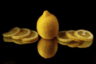 Whole lemon with lemon slices on the sides reflected in a mirror with a black background