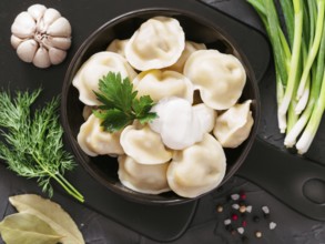 Traditional russian pelmeni, ravioli, dumplings with meat on black concrete background. Top view or