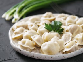 Traditional russian pelmeni, ravioli, dumplings with meat on black concrete background. Russian
