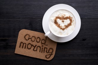 Porcelain cup of coffee with ice cream and cinnamon heart served at black wooden table