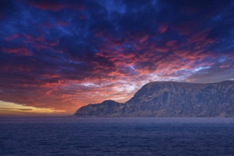 View from the sea to the West Cape in Norway at sunset with sun rays and heavy clouds. Waves in the