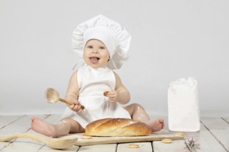 Child cooking. Beautiful little girl in cooking clothes with a long loaf of bread and flour. The