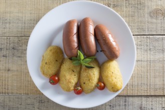 Pork sausages and breaded potatoes fried in a dish and decorated with cherry tomato placed on
