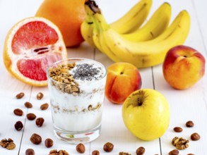 Healthy breakfast: yogurt with muesli and chia seeds, fruits and nuts on white wooden background.