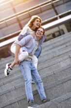 Man giving his pretty girlfriend a piggy back at street smiling at each other on a sunny day