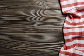 Red checkered napkin on brown wooden kitchen table with copy-space. Top view