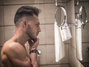 Shirtless muscular handsome young man looking at himself in bathroom mirror in the morning