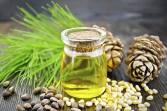 Cedar oil in a glass jar, two cedar cones, nuts and green twigs on a dark wooden board background