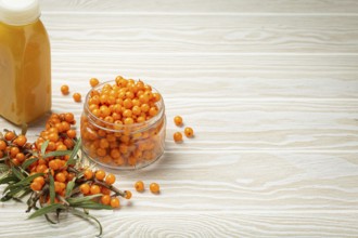 Sea buckthorn healthy drink in bottle, ripe berries in glass jar and branches with leaves top view