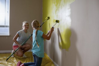 Two kids are joyfully and creatively painting a wall a bright yellow color, showcasing their