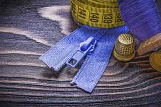 Vintage spool of thread measuring tape thimbles zip fastener on wooden board needlework concept