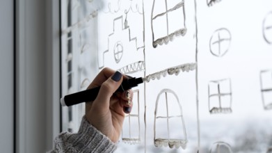 Female hand draws christmas holidays decoration painted on window glass. New Years scenery. city