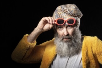 An elderly man with a grey beard wearing a knitted hat and a bright yellow fur coat. Fashionable