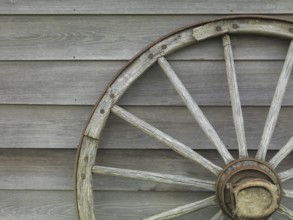 Old wooden cart wheel propped against a barn wall