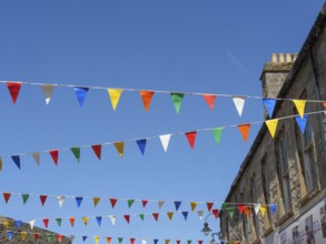 Colourful flags hang over a street corner between historic buildings under a cloudless blue sky,