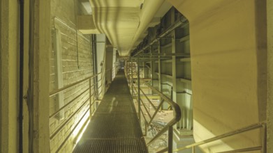 Industrial interior with a raised walkway and metal grating, surrounded by pipes and railings, Bad